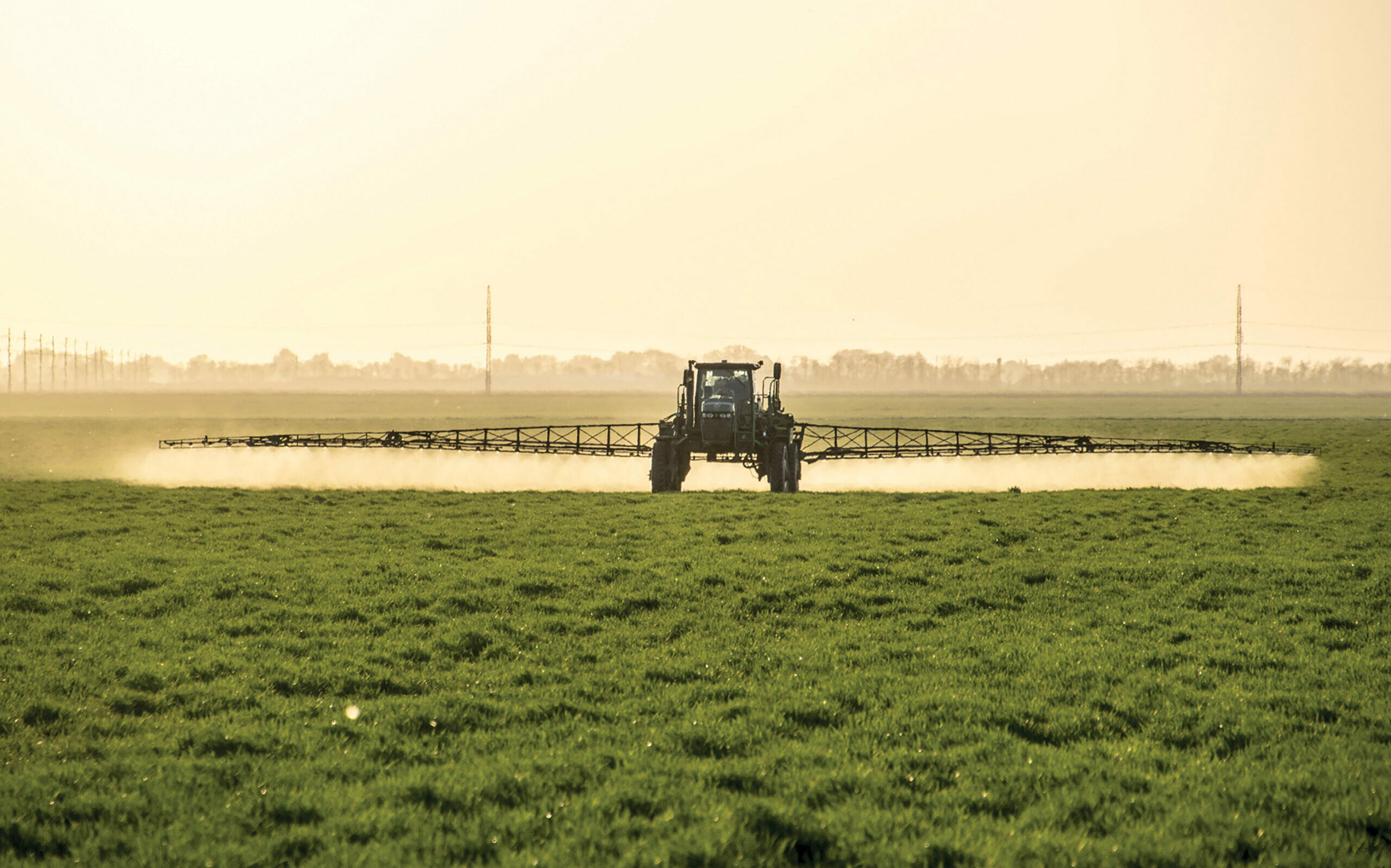 A tractor with a boom arm sprays crops.